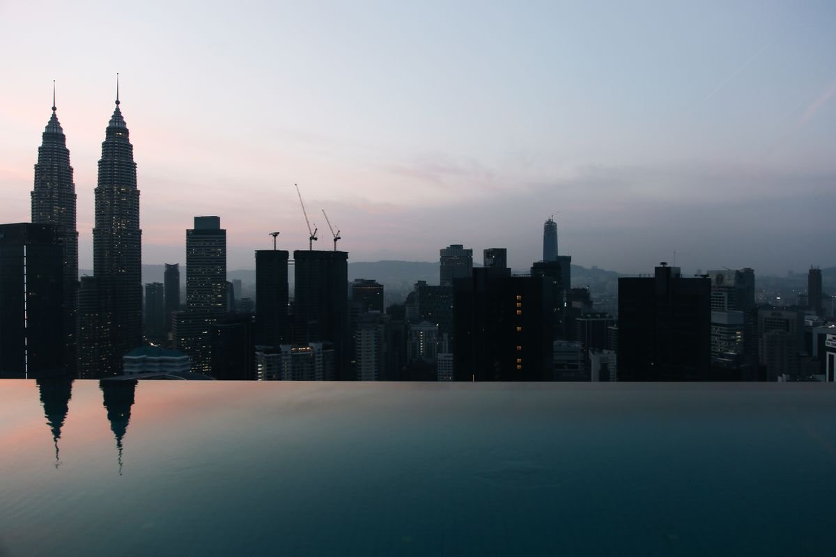 Kuala Lumpur skyline at dusk with the Petronas Twin Towers reflected in a rooftop infinity pool